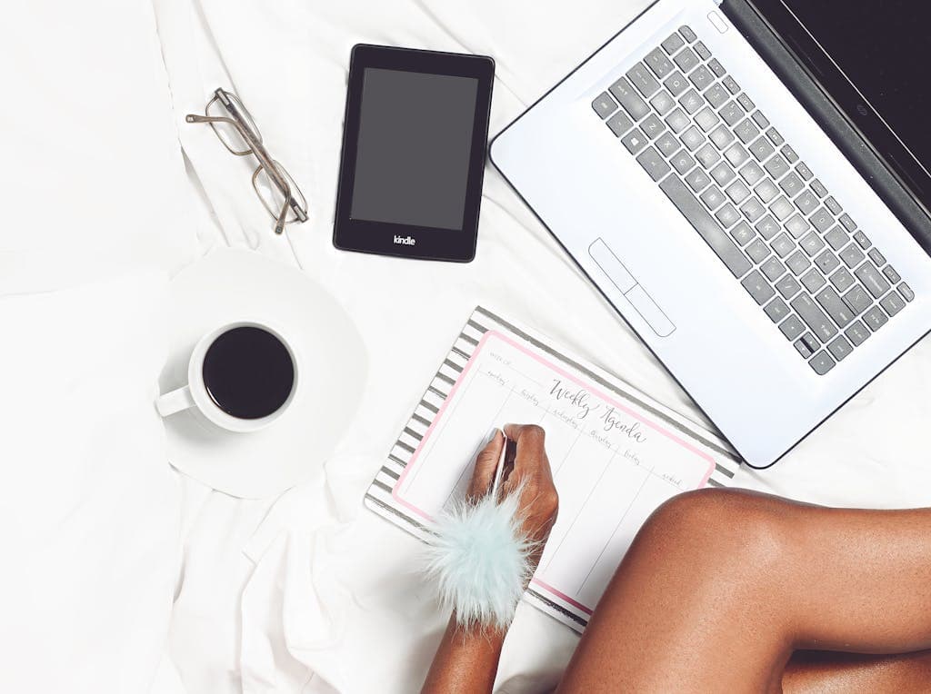 Flat lay of a cozy workspace with a coffee cup, laptop, Kindle, and planner for productivity.