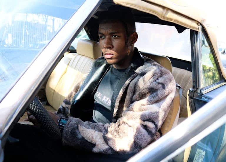 Stylish man in fur coat driving a vintage car on a sunny day.