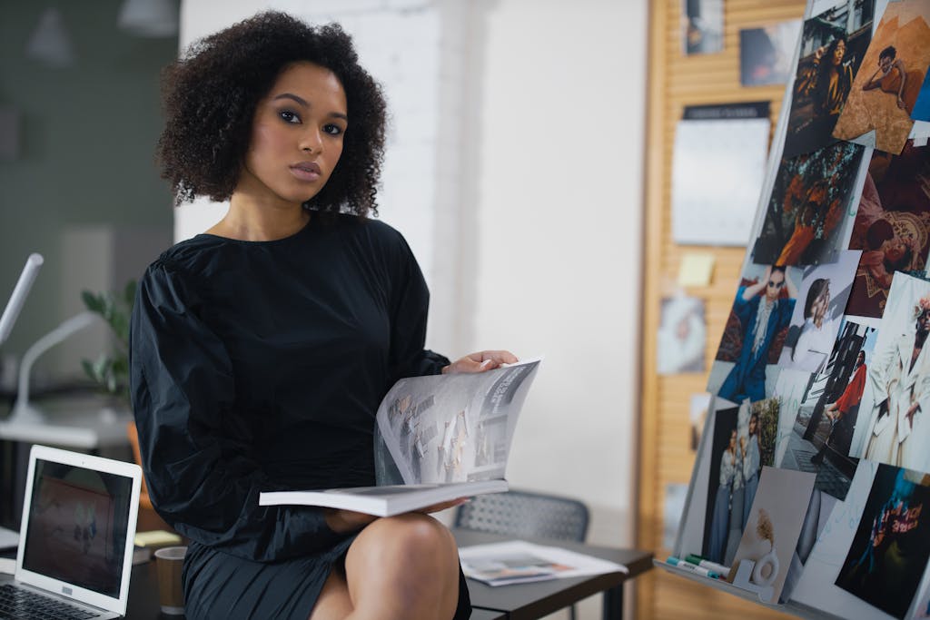 Elegant woman in a black dress holding a magazine in a modern office environment.