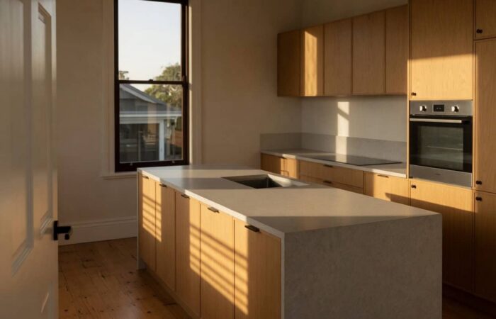 Handleless oak kitchen with a stone waterfall island and integrated sink in morning light