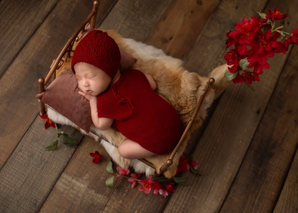 newborn baby posed side lying on a red prop bed