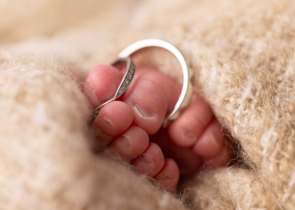 Macro photos of little toes holding parents' rings for newborn photography in Edmonton