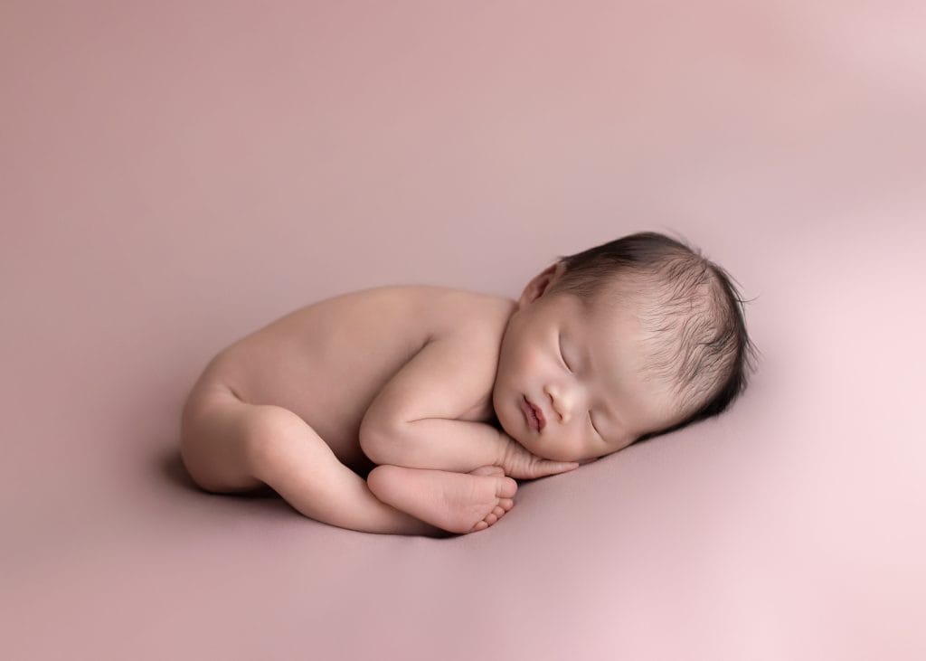 Classic posed newborn portrait with baby resting on soft pink fabric.
