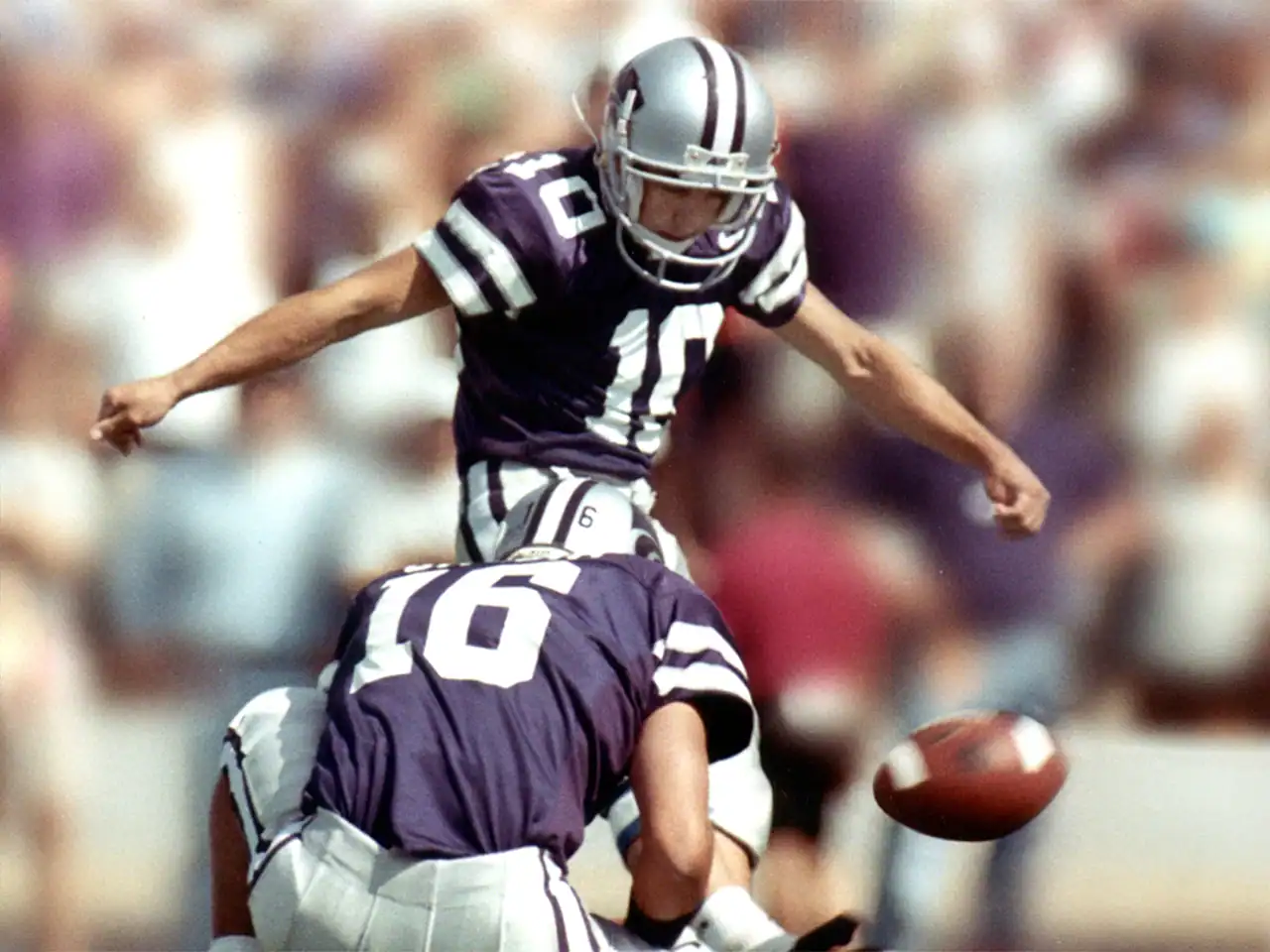 Football player kicking the ball during a game with a crowd in the background.