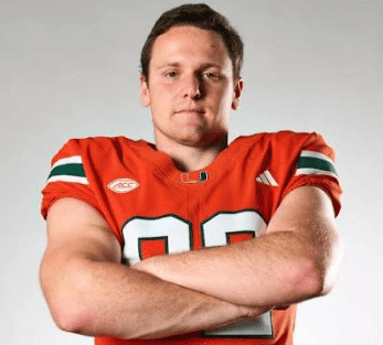 Football player in orange jersey with arms crossed, looking confident.