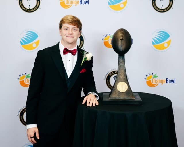 Young man in tuxedo with bow tie standing next to Lou Groza Award trophy.