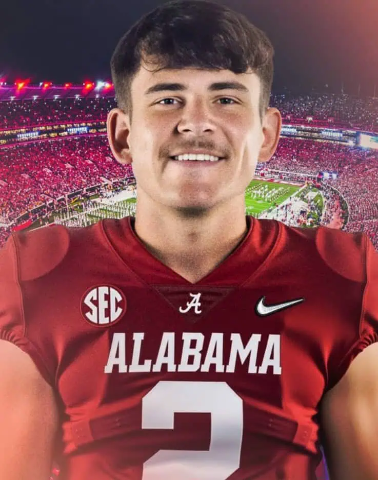 Alabama football player in red jersey at night game with stadium lights in background.