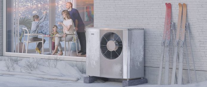 Modern heat pumps outside a home and covered in snow.