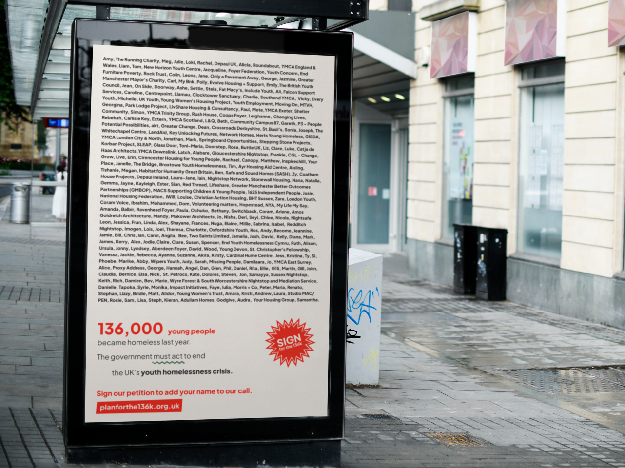 A bus stop on a city street showcases an advert addressing youth homelessness. The poster prominently displays a lengthy list of names at the top, presents statistics highlighting 136,000 young people experiencing homelessness, and includes an invitation to sign a petition to resolve the crisis.