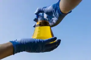 1. Laboratory glassware with yellow liquid being handled with blue gloves outdoors.
