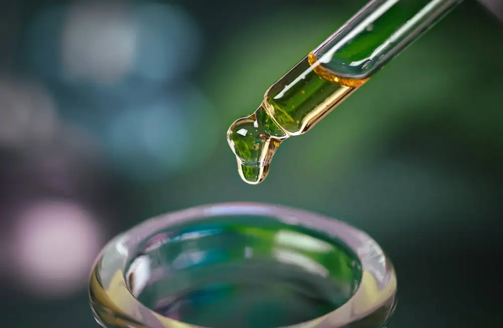 CBD oil dropper above a glass container, close-up of CBD extraction process.