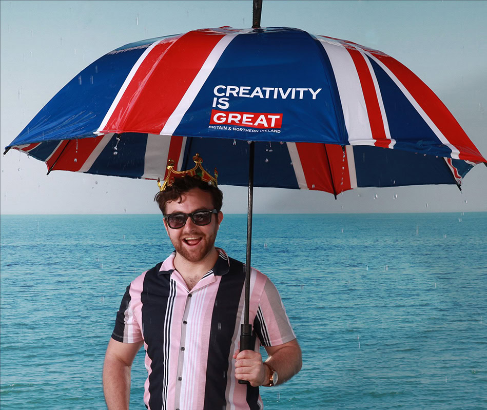 A studio portrait of a woman in a white tank top and black pants, standing with her arms crossed, illuminated by distinct red and blue/purple lighting.