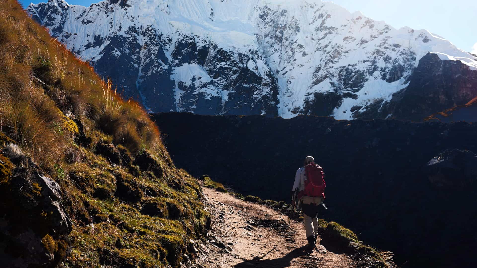 Hiker trekking along mountain trail with snow-capped peaks in Cusco, Peru.
