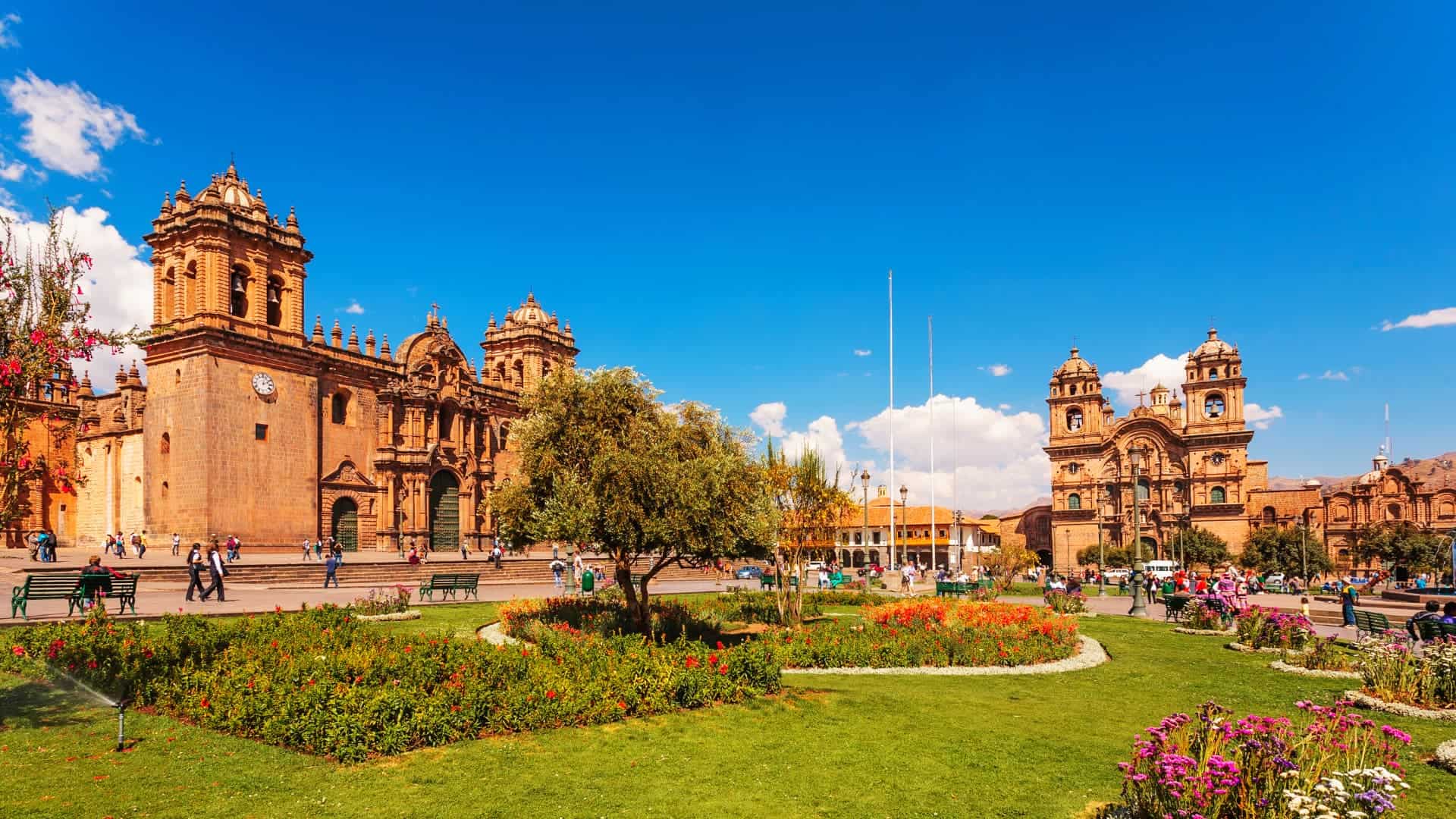 A vibrant view of Cusco’s Plaza de Armas with its lush gardens and colonial architecture under a bright blue sky- Magical Cusco Travel Agency