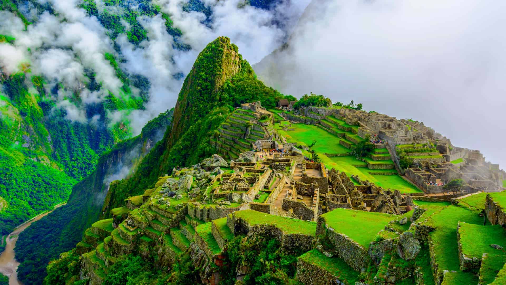 Stunning aerial view of Machu Picchu with green terraces, ancient stone structures, and mist-covered mountains – Cusco to Machu Picchu, Cusco Magical Travel Agency and panoramic view of Machu Picchu from upper terraces