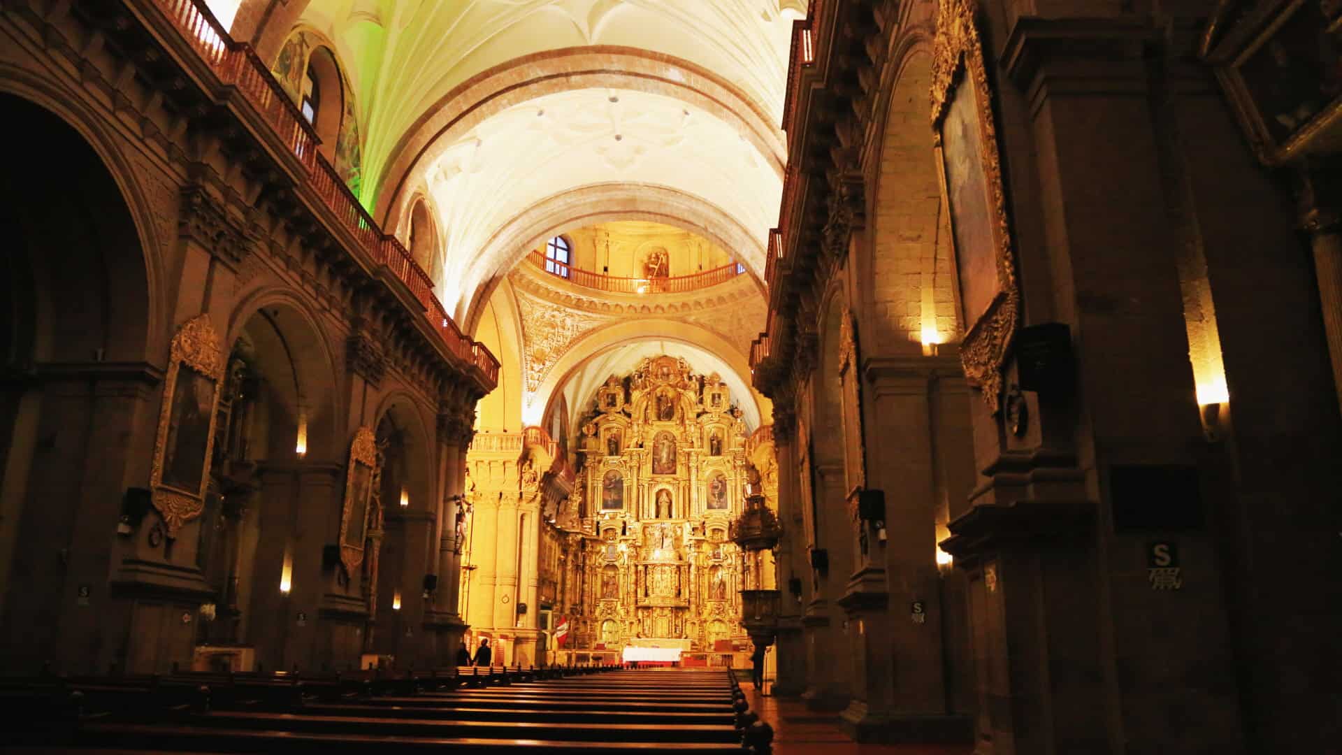 A breathtaking view of the richly decorated interior of a historic cathedral, featuring golden altars and high arched ceilings.