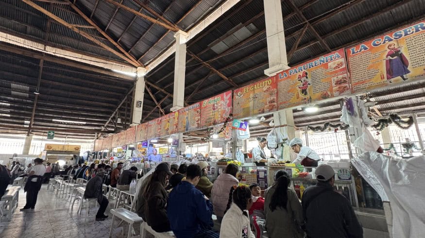 Bustling Cusco market with local vendors, tourists, and colorful food stalls in a vibrant setting.