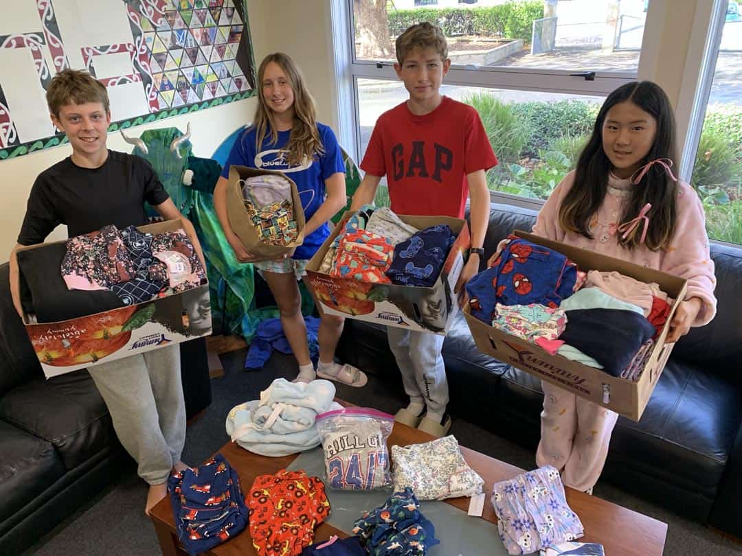Brightly dressed students at Mangorei School holding boxes of donated clothing and pajamas.