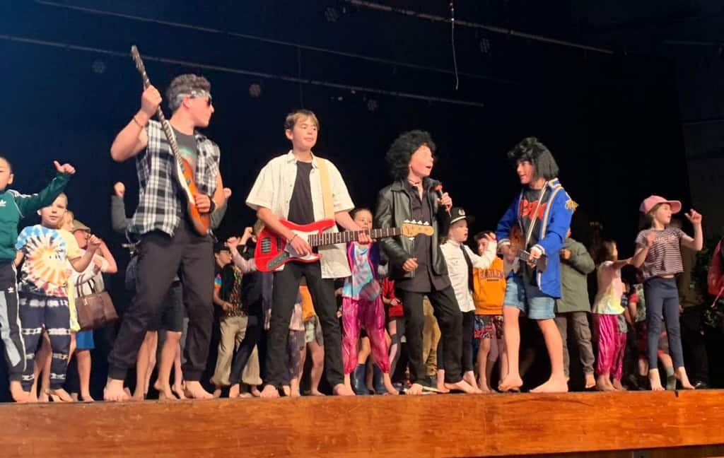 Vibrant school concert at Mangorei School showcasing students performing on stage with musical instruments and costumes.