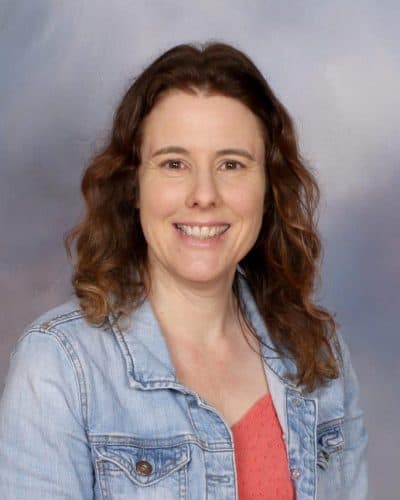 Smiling woman with brown curly hair wearing a denim jacket for Mangorei School staff profile.