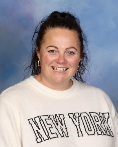 Smiling woman wearing a 'New York' sweater against a blue sky background.