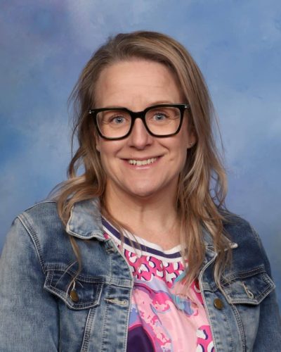 Bright smiling woman wearing glasses and denim jacket at Mangorei School, New Zealand.