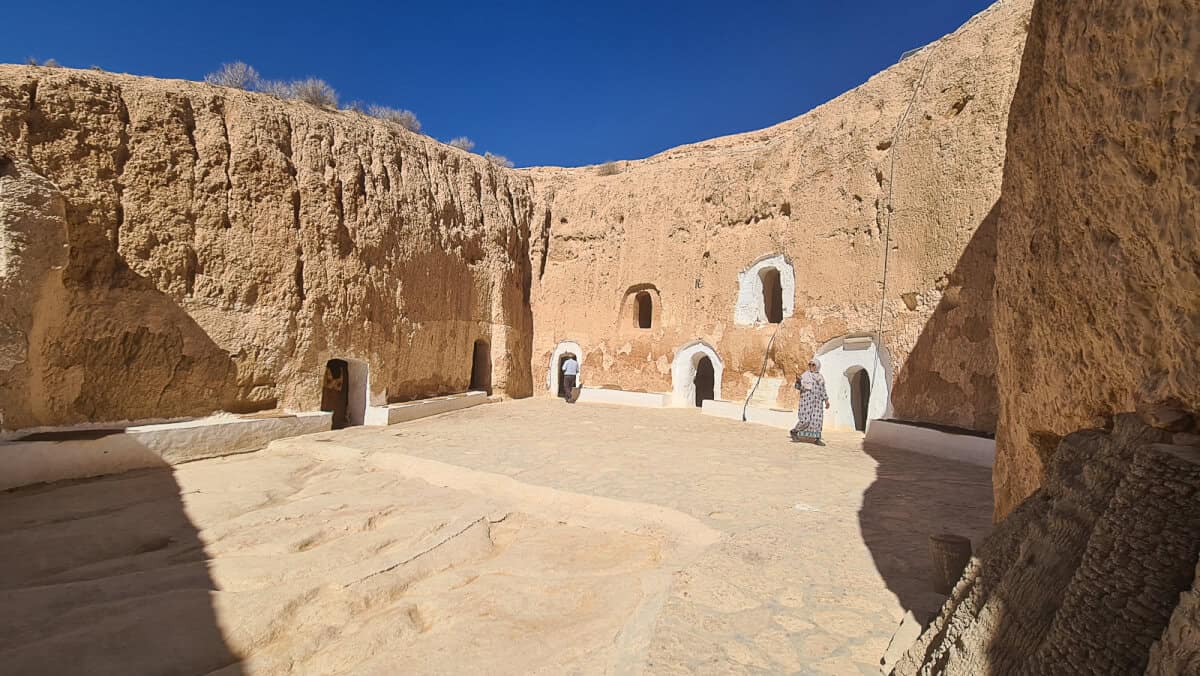 Traditional troglodyte house in Matmata, Tunisia, with rooms carved into the earth around a sunken courtyard. The image shows arched doorways leading into underground Berber homes, a unique example of ancient North African architecture adapted to the harsh desert climate, and popularized as a Star Wars filming location.