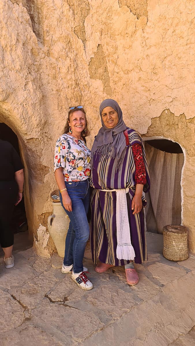 Maria Dol of Map and Camera posing with a local Berber woman in traditional striped dress outside a troglodyte house in Matmata, one of the top cultural places to visit in Tunisia.