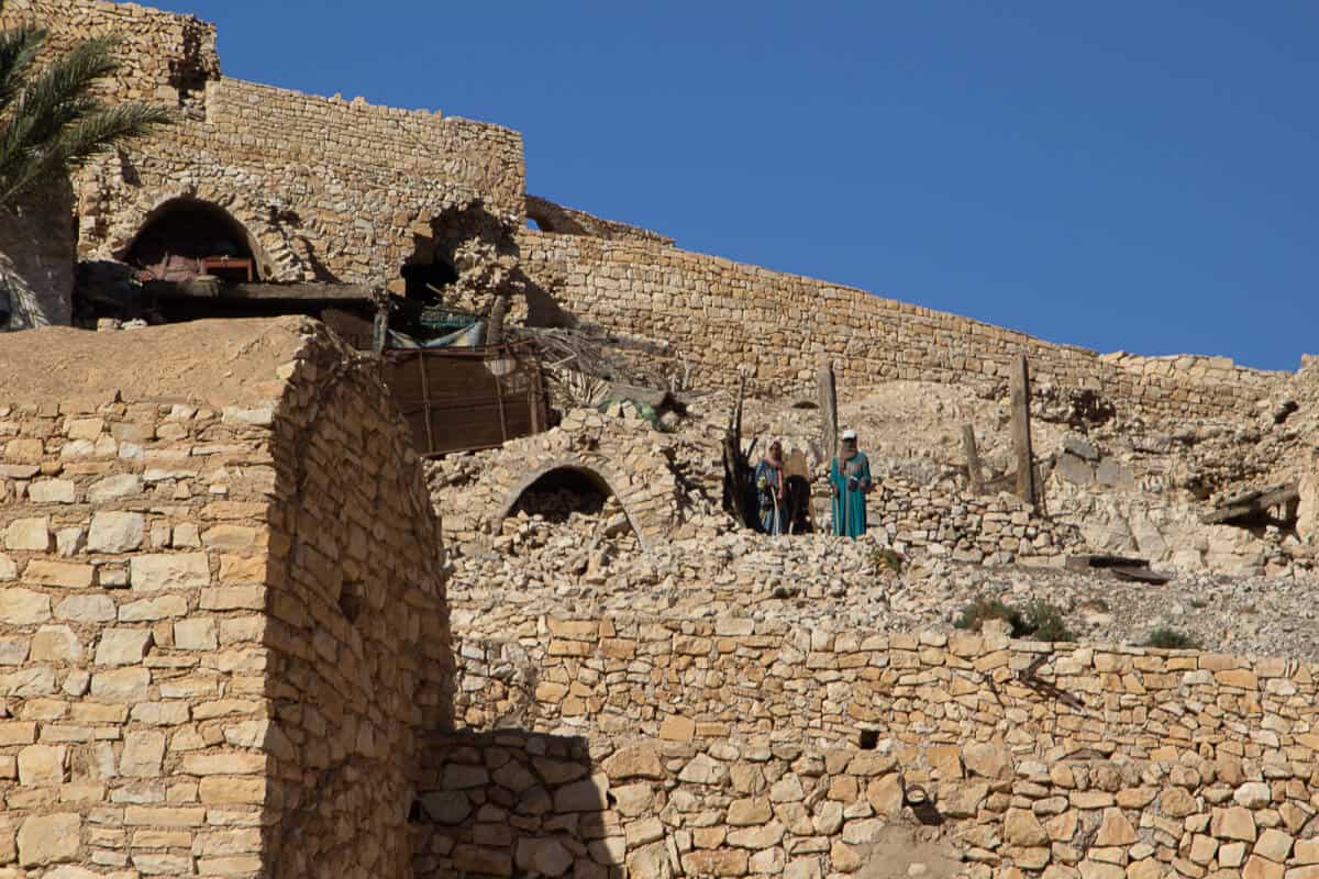 View of Beni Zelten village built from stone on a hillside in southern Tunisia, showcasing authentic Berber architecture and local men in traditional attire.