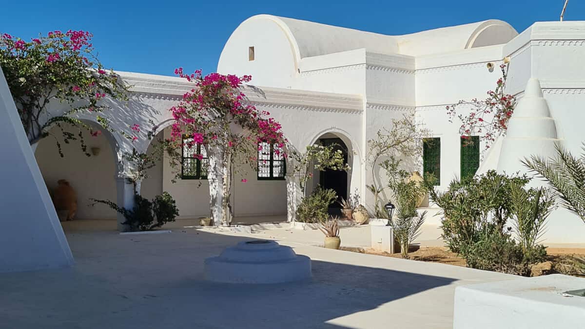 Traditional Tunisian architecture with white domed roofs and blooming bougainvillea at Guellala Museum, a top spot to explore Berber heritage on Djerba Island.