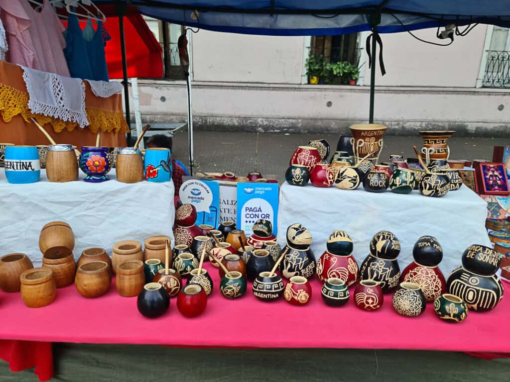 A vibrant market stall at Mataderos Fair in Buenos Aires showcasing handcrafted mate gourds with intricate carvings and designs, alongside traditional wooden mate cups. These unique Argentine souvenirs reflect the country's rich cultural heritage.