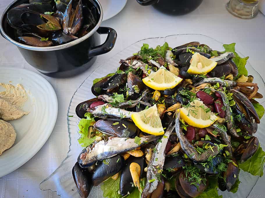 A platter of mixed seafood, consisting of mussels with their shells slightly open, and small fish. The seafood is arranged on a bed of fresh lettuce.