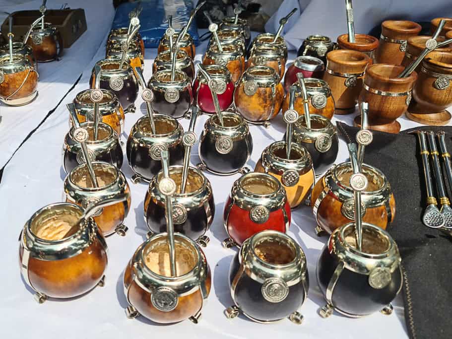 A variety of handcrafted Argentine mate sets with silver details, including traditional gourds and bombillas, displayed at a Buenos Aires market. A perfect souvenir for experiencing Argentina's mate-drinking culture.