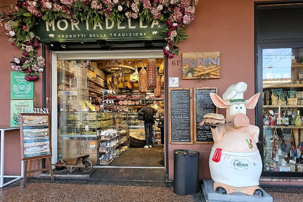 Traditional Bologna deli shop near Bologna Centrale featuring mortadella and panini, with iconic pig statue — a must-see local food stop in Bologna, Italy.