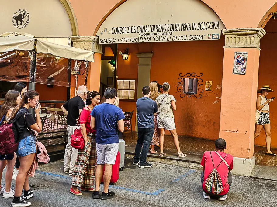Tourists lining up to peek through La Finestrella di Via Piella, a must-see hidden window into Bologna’s canal system, popular among photographers and Instagram users.