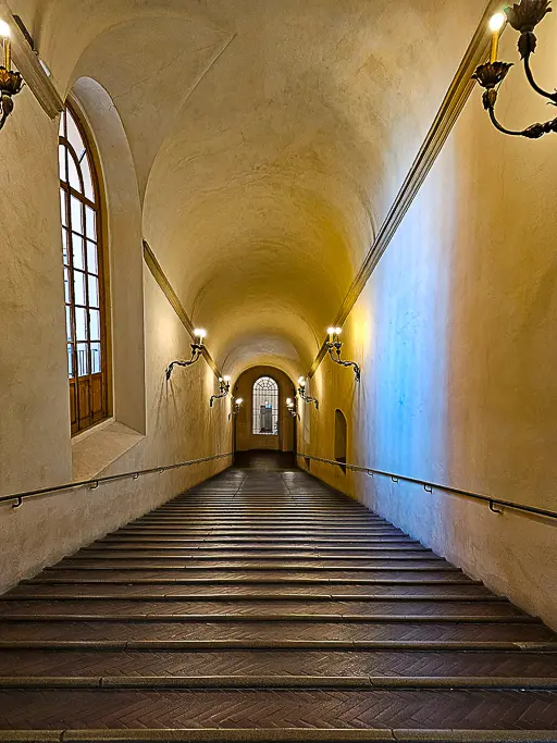Elegant stone staircase inside Palazzo d'Accursio in Bologna, illuminated by antique sconces and arched ceilings—ideal for capturing moody interiors and historical architecture.