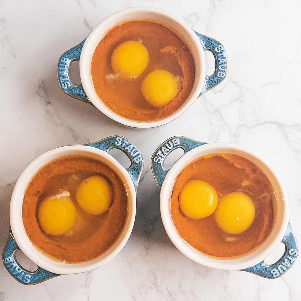 3 mini cocotte dishes with eggs and tomato sauce.