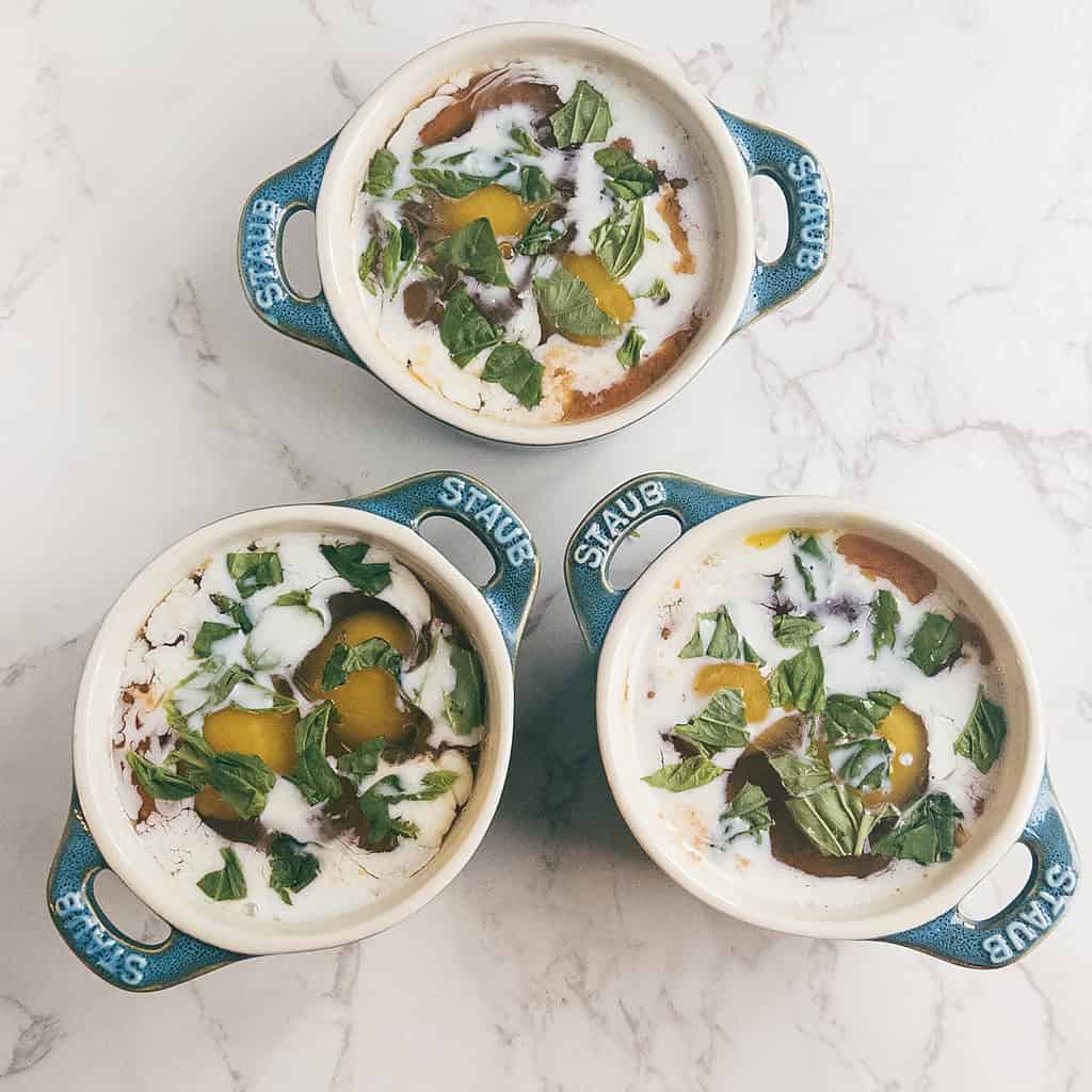 3 mini cocotte dishes with eggs, tomato sauce, fresh basil, and a splash of cream.