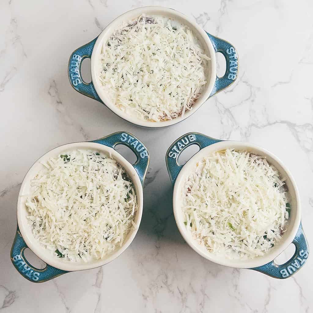3 mini cocotte dishes with shredded parmesan cheese over eggs in tomato sauce.