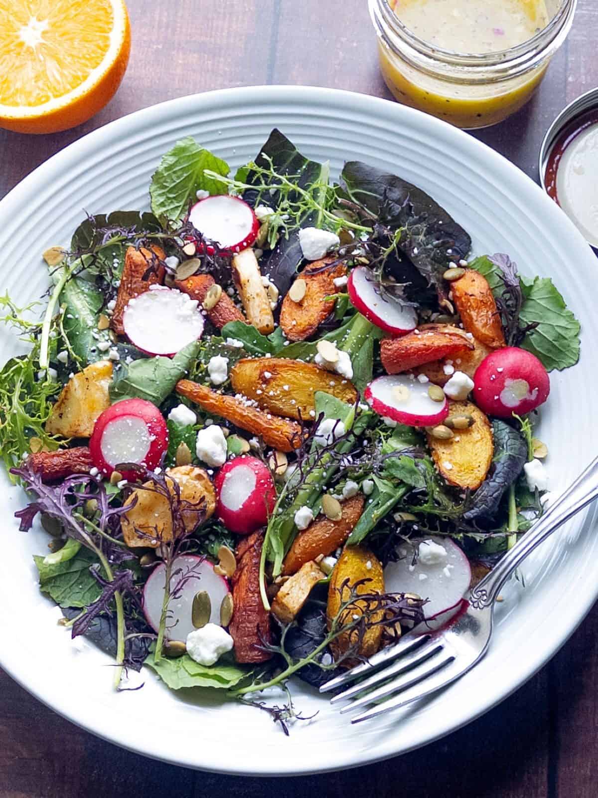 finished-salad-in-large-rimmed-bowl-with-sliced-orange-and-dressing-jar-in-background