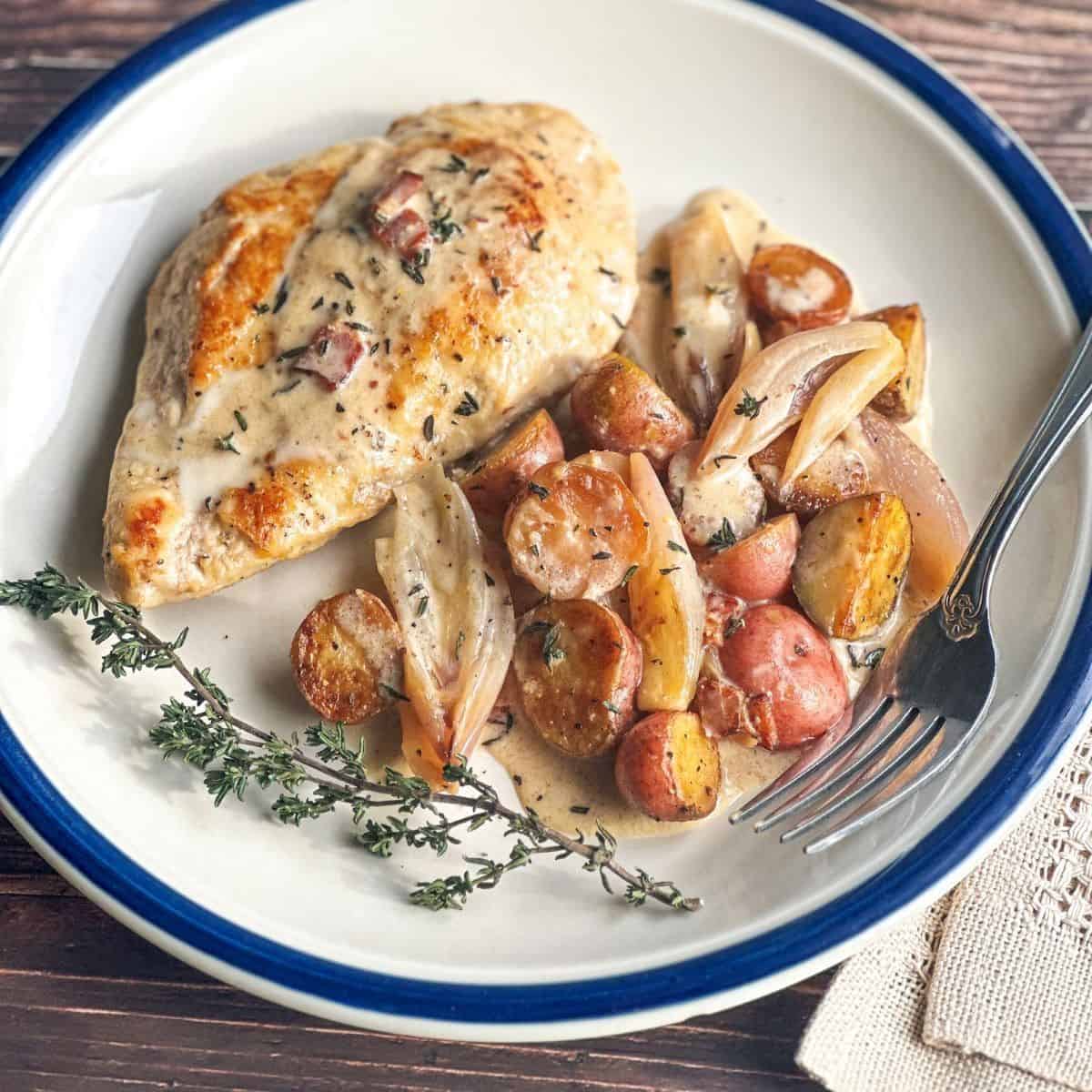 Chicken breast with shallots and potatoes on a round white plate.