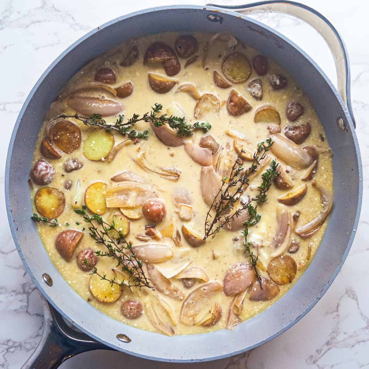 potatoes, shallots, hard cider, creme fraiche, and fresh thyme in skillet - process shot