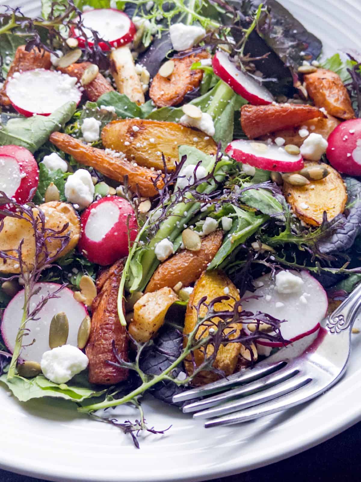 Carrots, parsnips, radishes, mixed greens, goat cheese, and pepitas with a fork in a bowl.