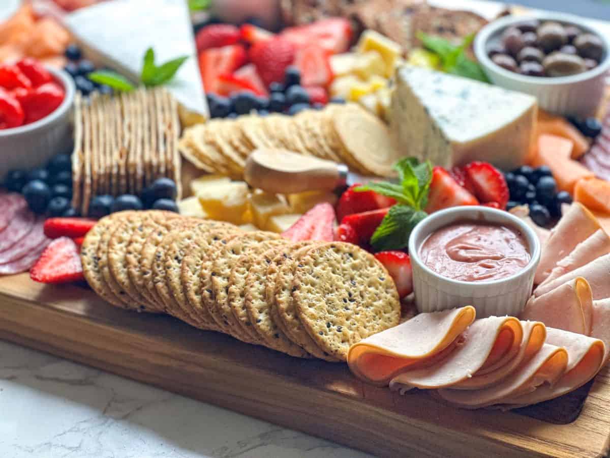 Charcuterie board with crackers, sauces, meats, and cheese.