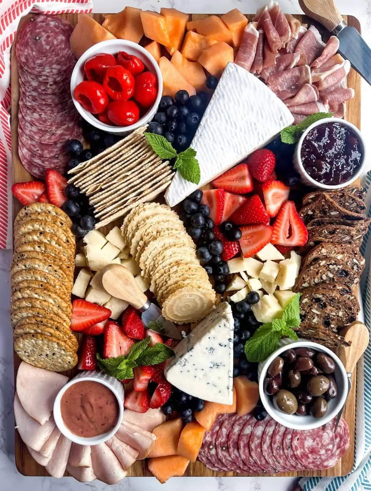 A large rectangular charcuterie board with meat, cheeses, fruit, olives, spreads, and crackers.