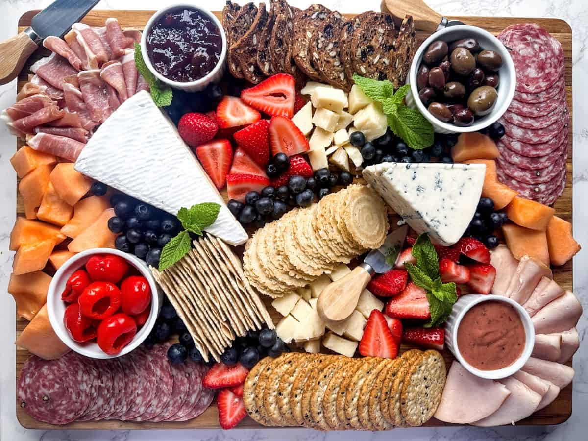 Large rectangular charcuterie board with meats, cheeses, crackers, fruit, and spreads.