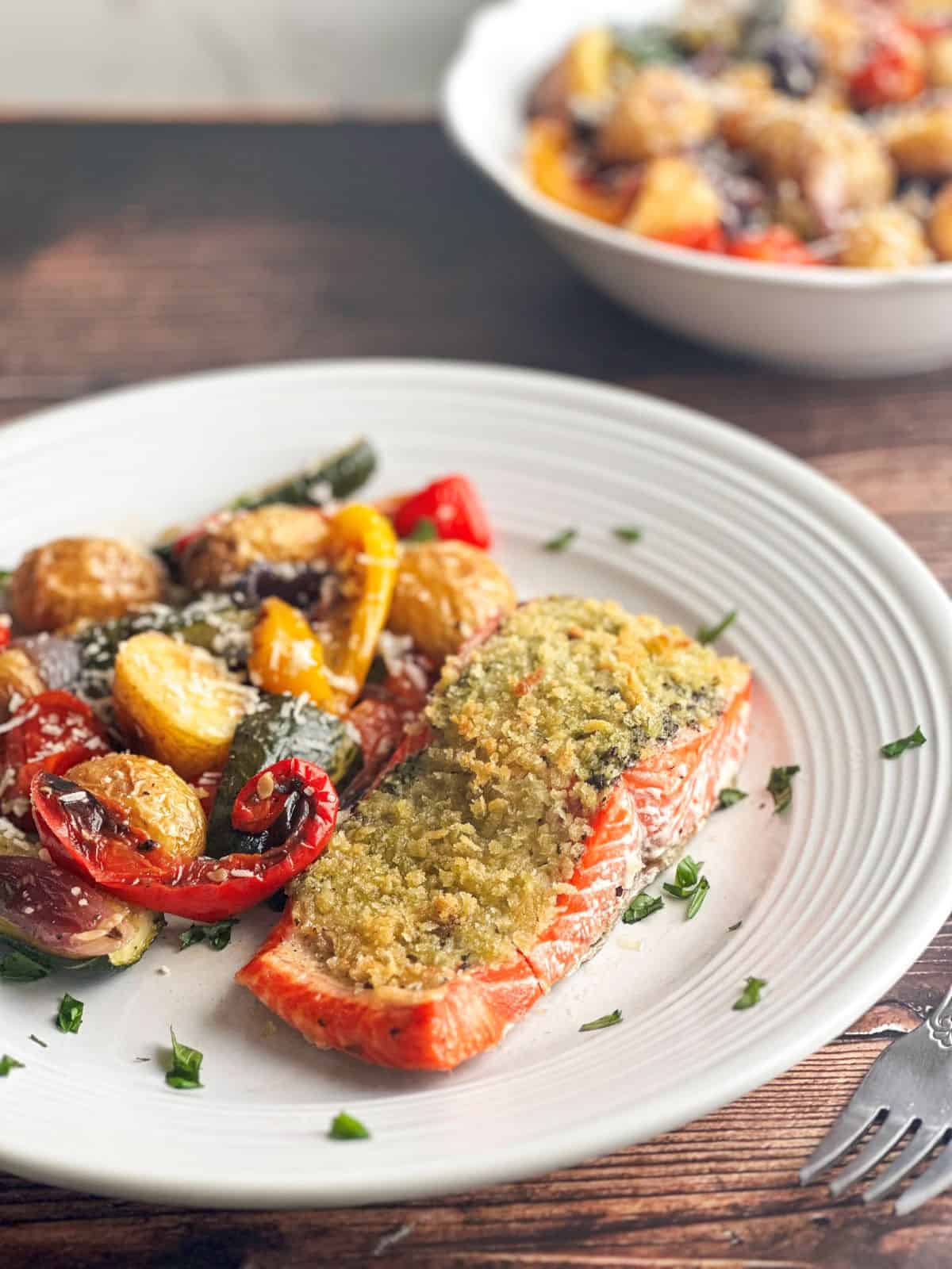 Salmon with pesto crust and roasted vegetables on a round white plate.