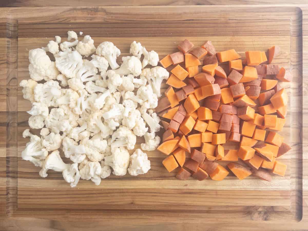 Chopped cauliflower and sweet potatoes on wood cutting board.