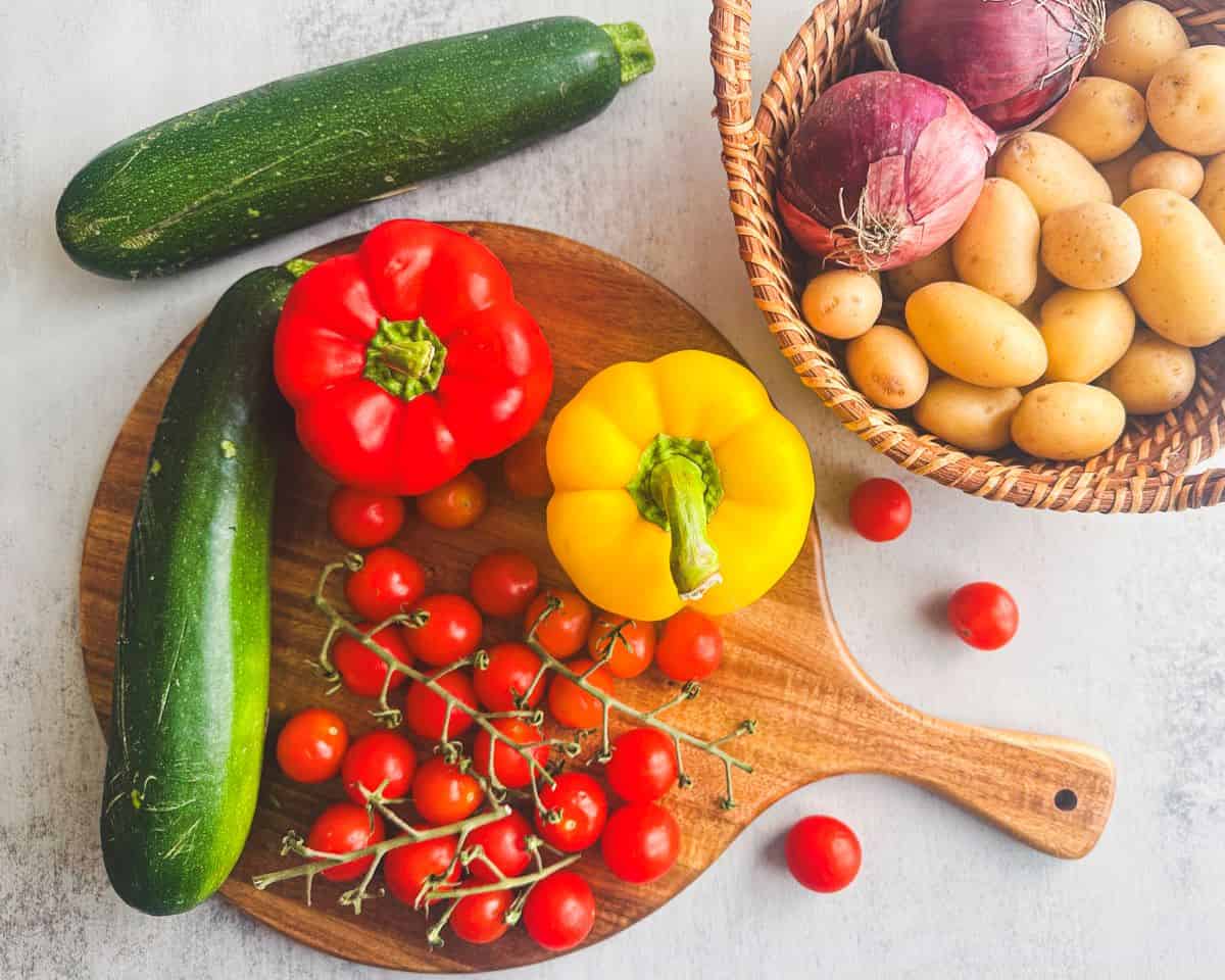 Ingredients for Italian-style roasted vegetables on a wood cutting board and in wooden basket.