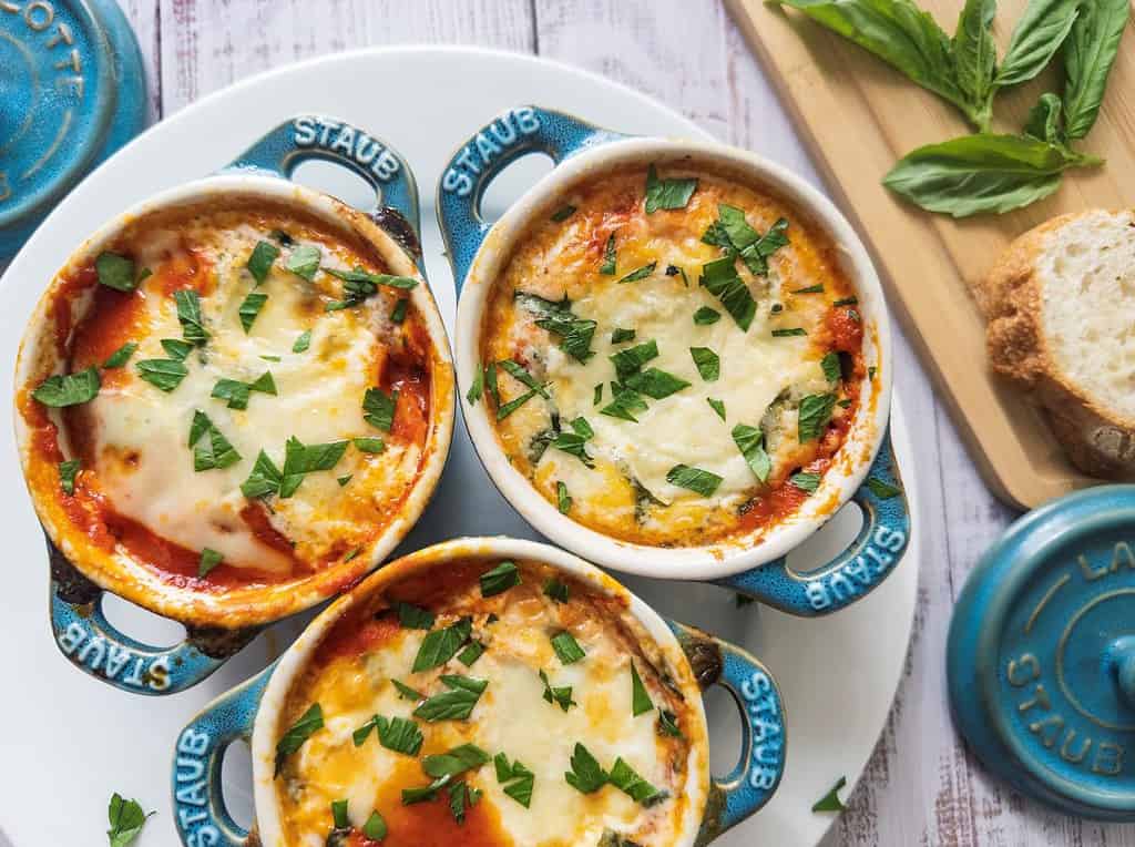 Baked eggs with cheese and tomato sauce in three small Staub cocotte dishes.